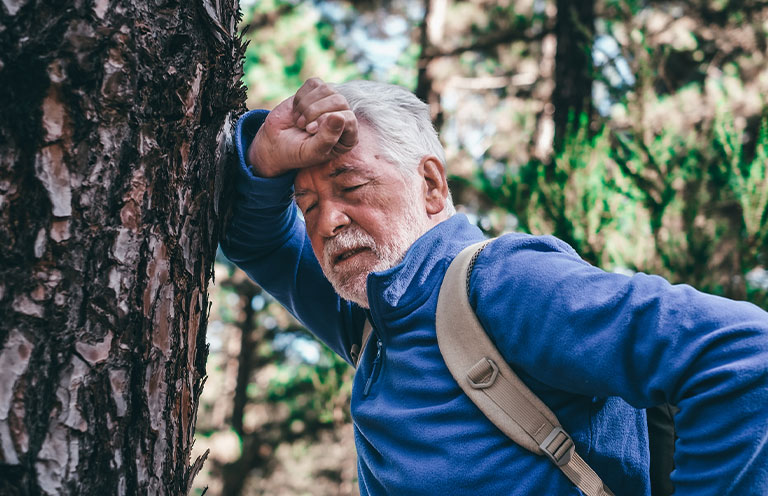 man with backpack breathless leans against a tree trunk
