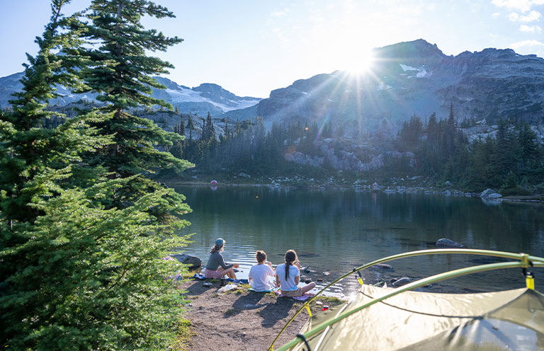 Mother and daughters eat dinner on lakeshore by campsite, Semaphore Lake, B.C.