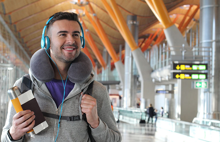 man wearing headphones, neck pillow, holding water bottle and passport at an airport