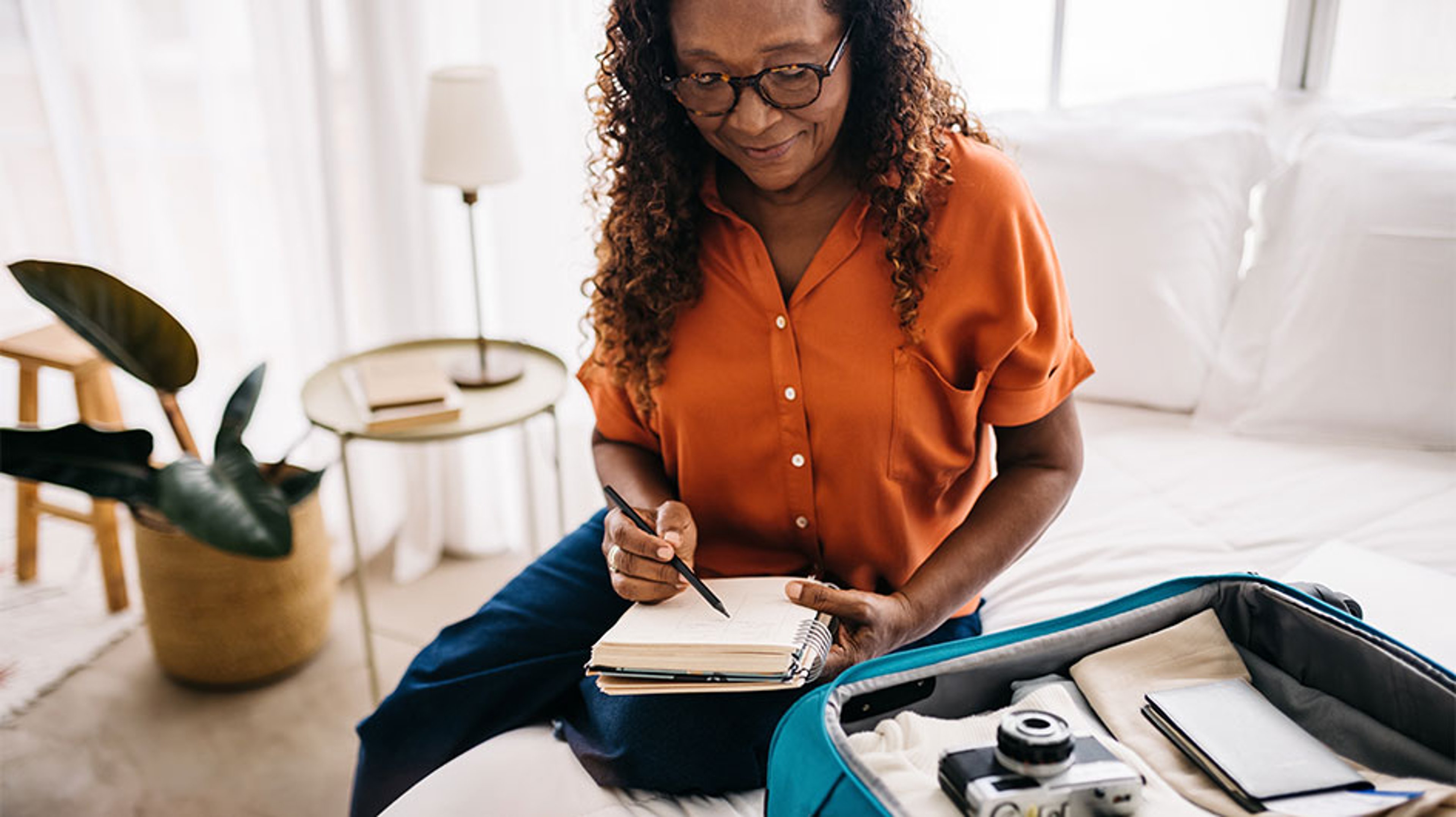 woman writing in notebook next to open carryon suitcase