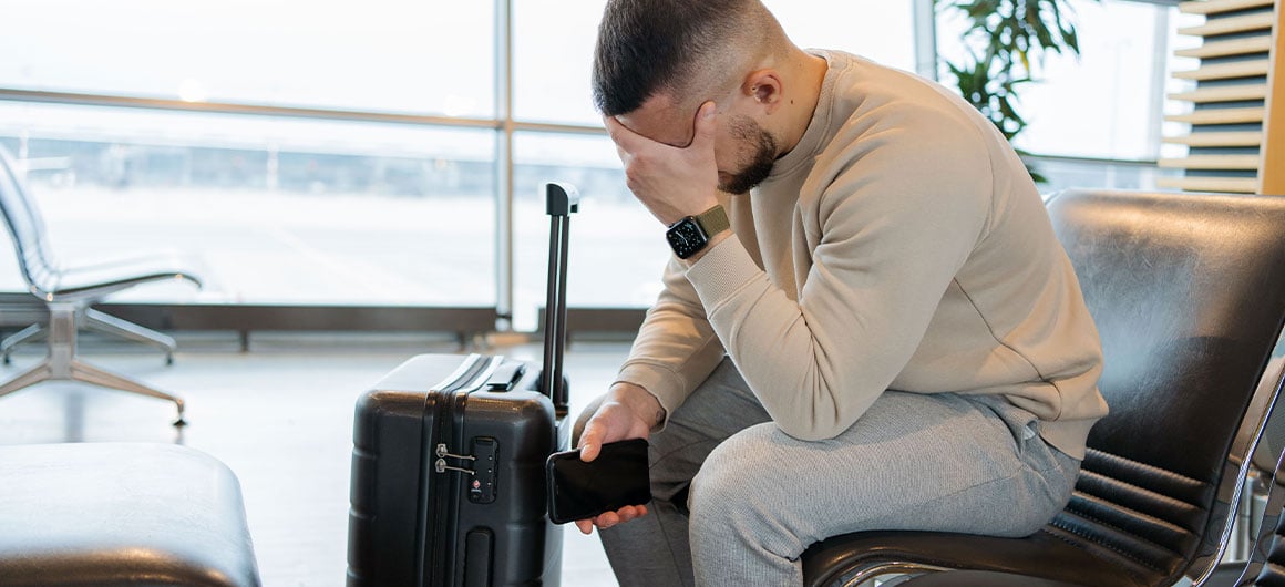 sad man at airport next to suitcase