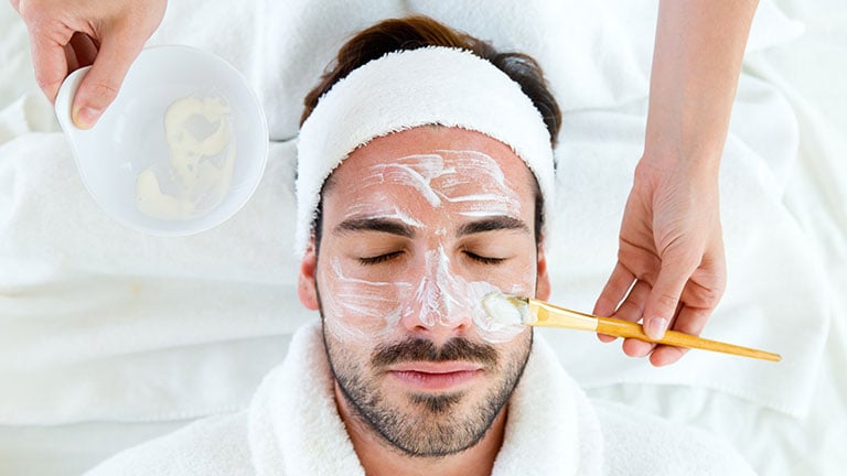 Man with clay facial mask in beauty spa. By nenetus