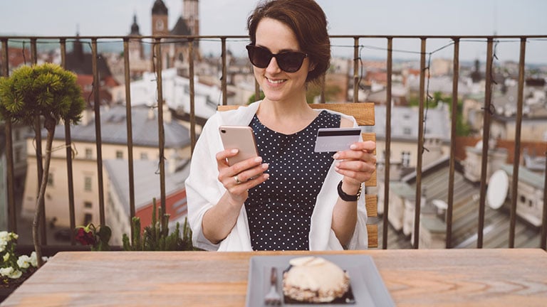 Young woman on rooftop restaurant using smart phone for online shopping; Credit: martin-dm