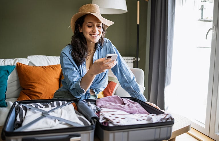 woman using phone while packing suitcase