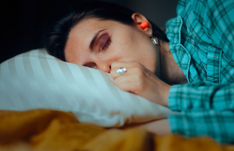 person laying in bed with earplugs in