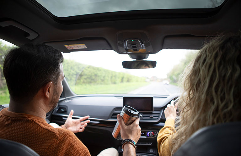 man in passenger seat of car holding coffee, woman driving