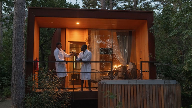 African American gay male couple enjoying a romantic resort weekend and beautiful evening, talking and drinking wine on a terrace. By 24K-Production