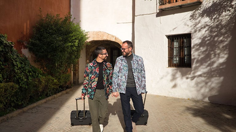 Real marriage of gay couple, holding hands, walking around the city with a travel suitcase in the other hand. Concept lgtb, lgtbiq+, couples, in love, travel. See Less By Manuel