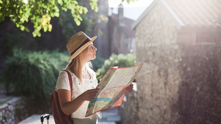 Girl traveler is using city map at town street. Woman tourist is searching direction, exploring locations, walking in magic light. Concept of travel, vacation, female tourism, adventure, trip, journey. By Marina April