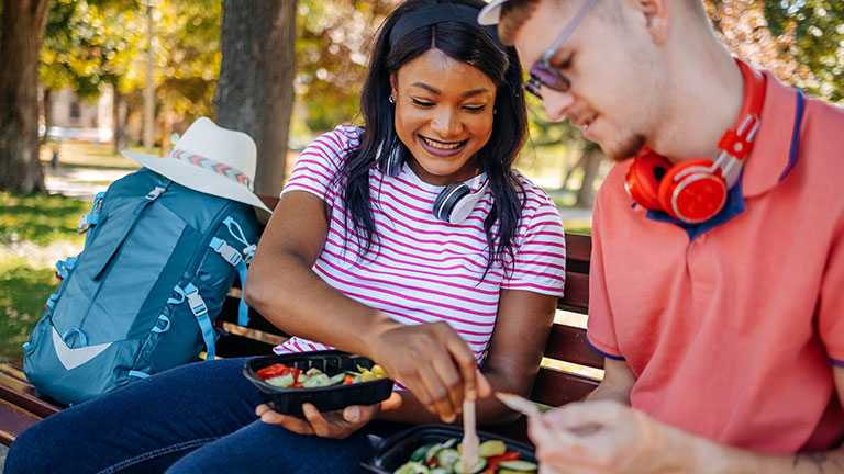 Multiracial couple enjoying visiting cities as a tourists in the summer resting in public park while having a meal together Credit: Dejan Marjanovic