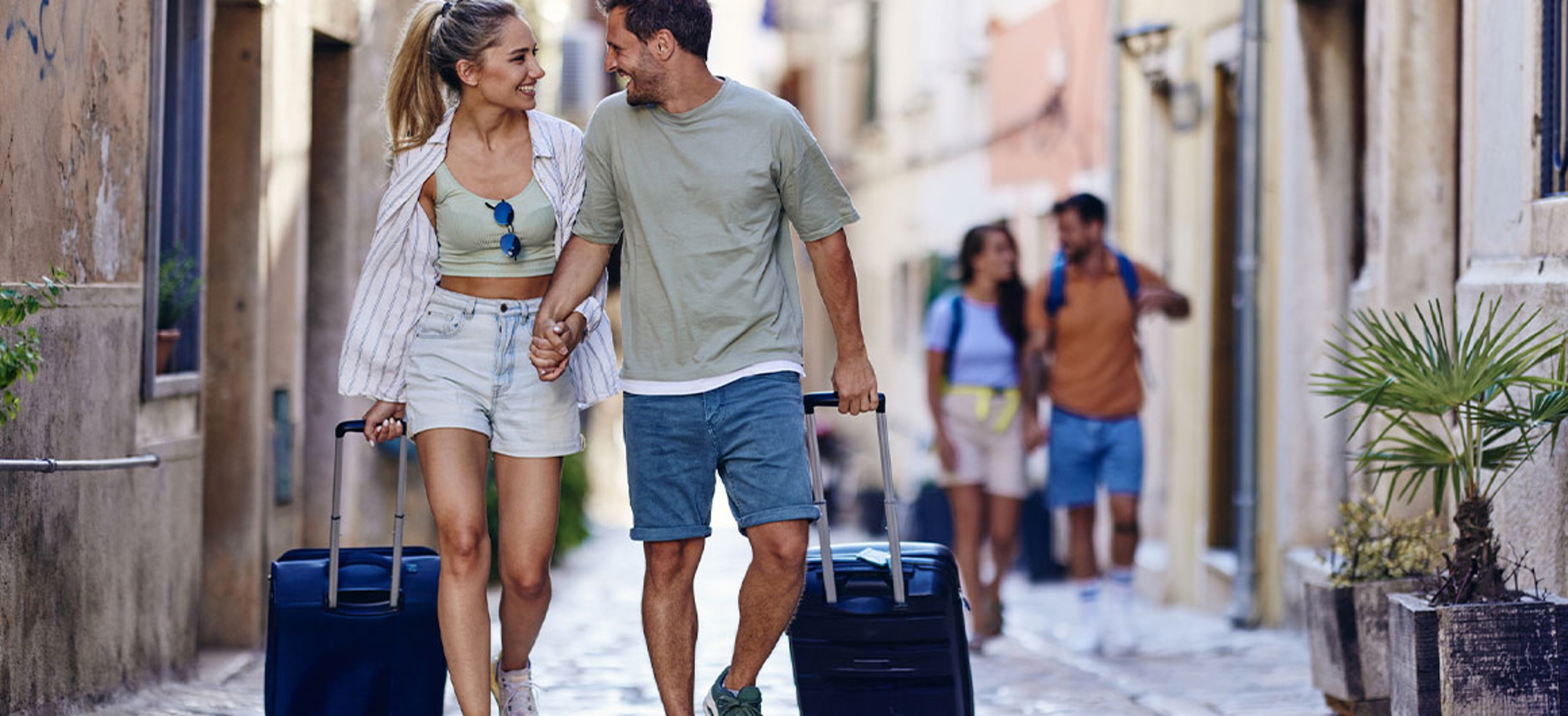 man and woman walking down cobblestoned street with suitcases