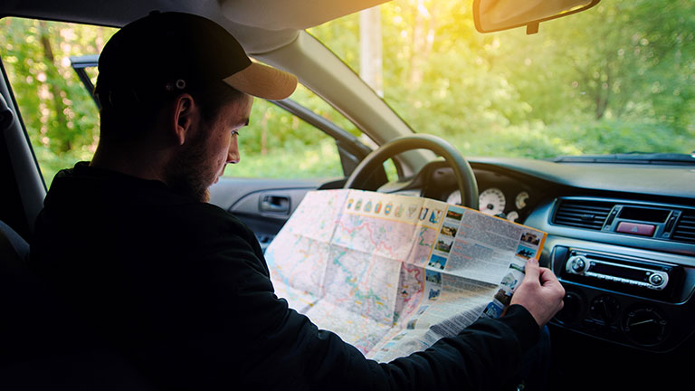 Losted in the forest young driver sitting in car while holding map and looking aside  by lisovoy