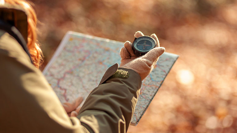 Woman holding a compass and reading a map while hiking  by Impact Photography