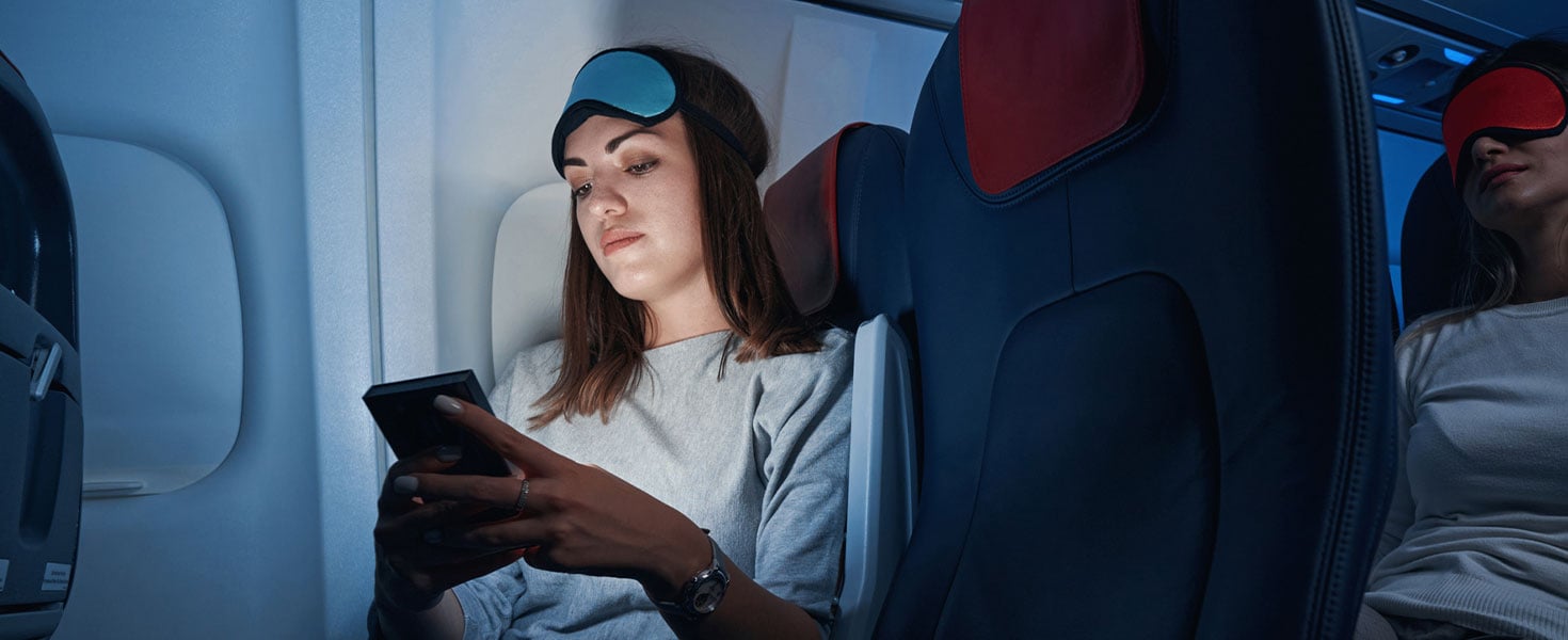 girl with eye mask on plane, using phone
