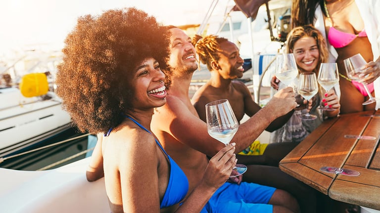 Multiracial friends having fun at boat party during summer vacation - Happy people cheering with champagne inside sailing boat at sunset - Travel and holidays concept - Main focus on african girl face. Credit: DisobeyArt