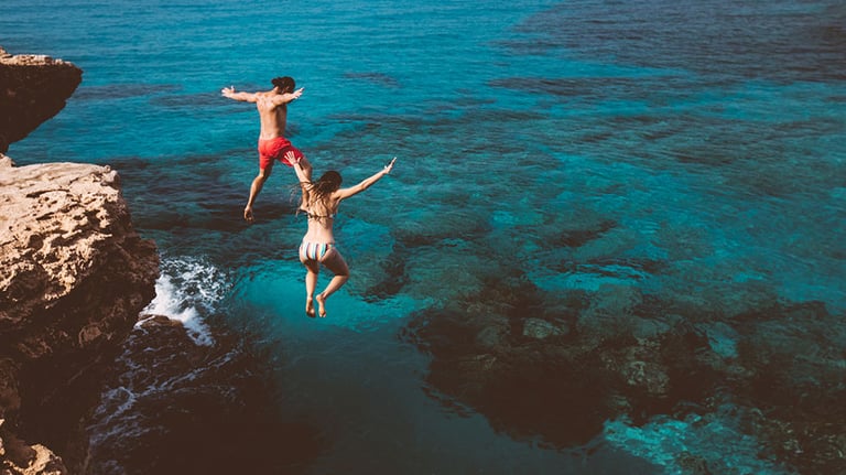 Young brave divers couple jumping off cliff into ocean. Credit: wundervisuals