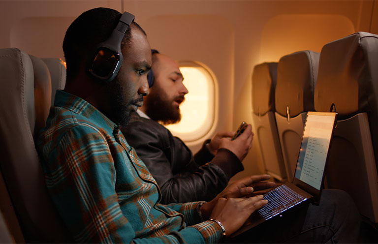 man wearing headphones and working on laptop on airplane
