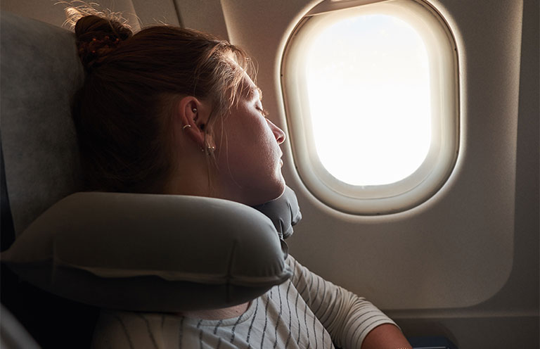 woman wearing neck pillow on airplane, leaning against window
