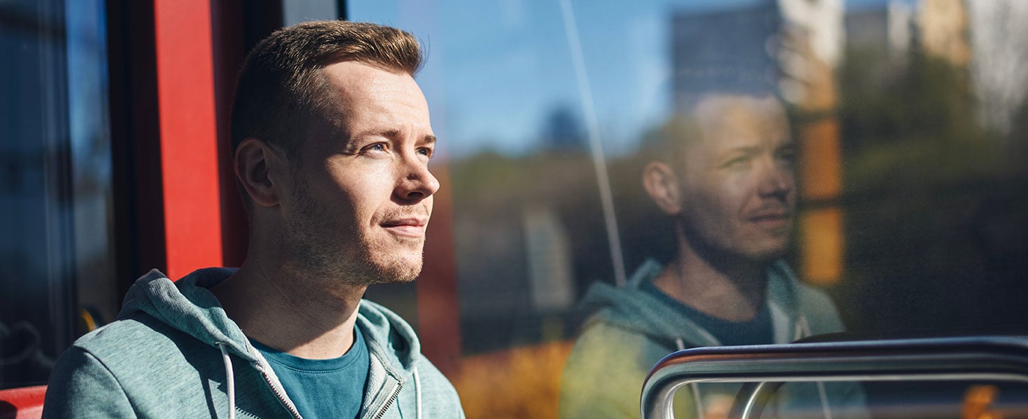 Man commuting by tram. Adult passenger looking out window of train of public transportation; by Chalabala