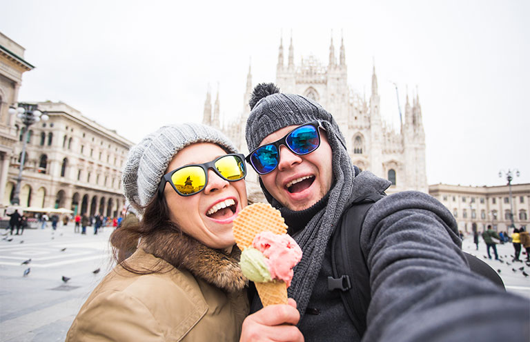 man and woman holding ice cream cone together wearing winter hats and coats in europe cloudy skies