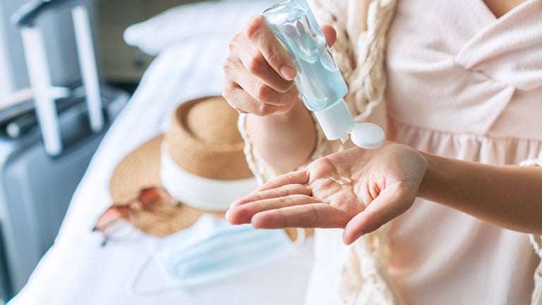  Downloaded Beautiful Asian traveler woman sitting on bed and apply sanitizer gel on her hands in hotel room. Travel, health care and new normal lifestyle concept.
