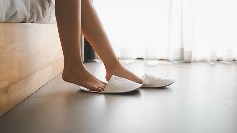 closeup woman legs with slippers sitting on bed
