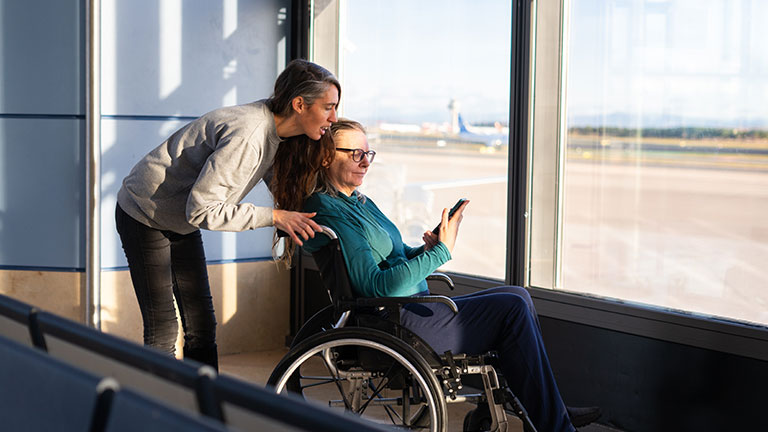 Passenger with disability using mobile phone assisted by airport staff By Arianne