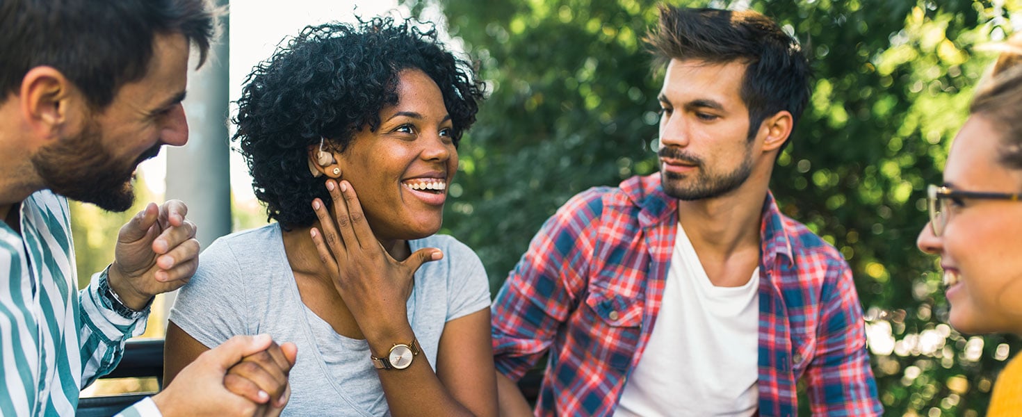 Woman with ear hearing problem having fun with her friends in the park By Mediteraneo