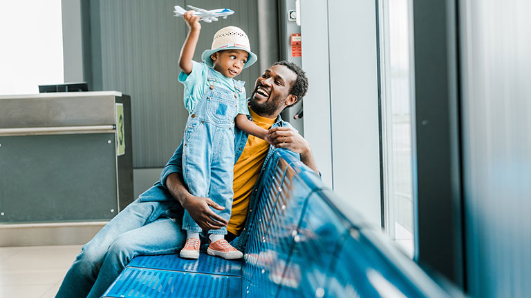 happy african american father looking at son while boy playing with toy plane in airport by LIGHTFIELD STUDIOS