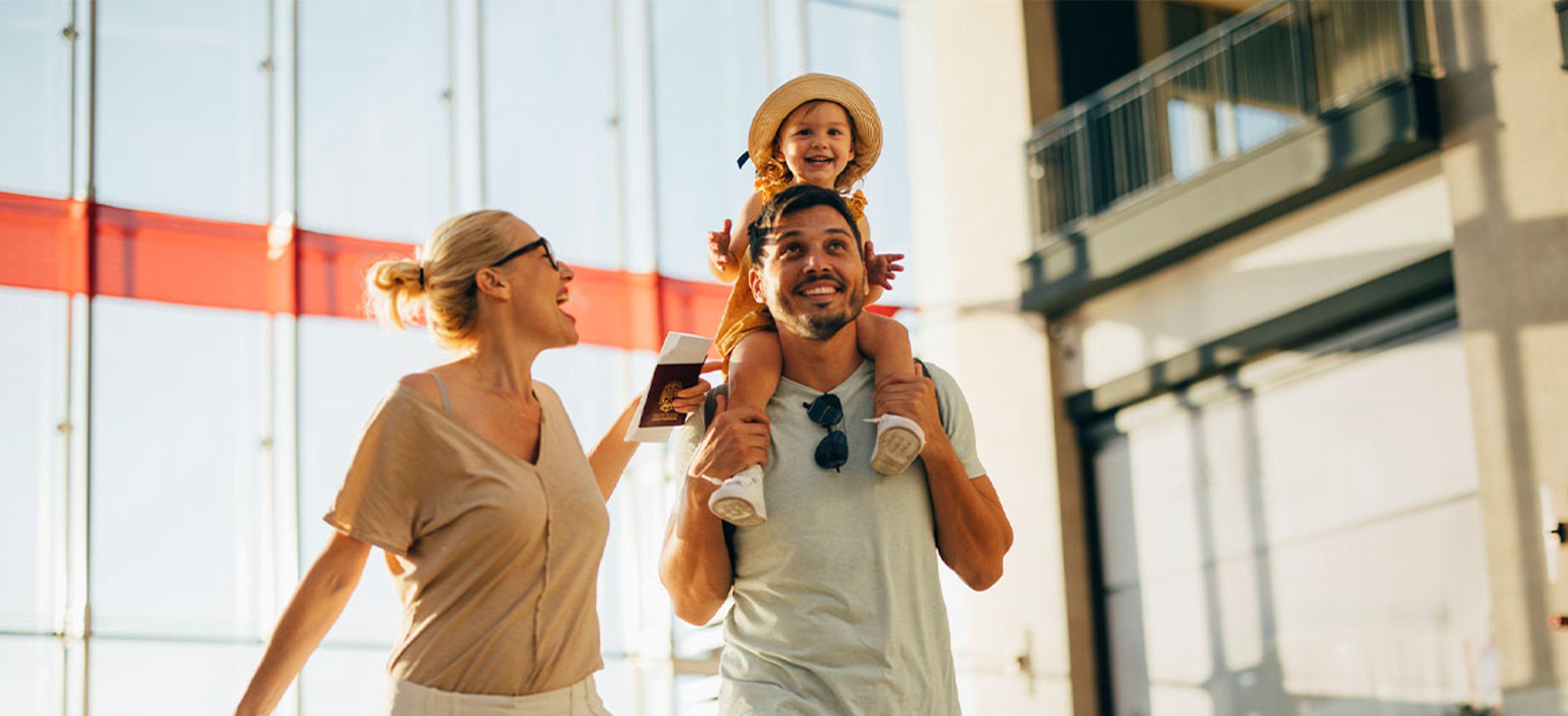family of 3 walking in airport, child on dad's shoulder, mom holding passport
