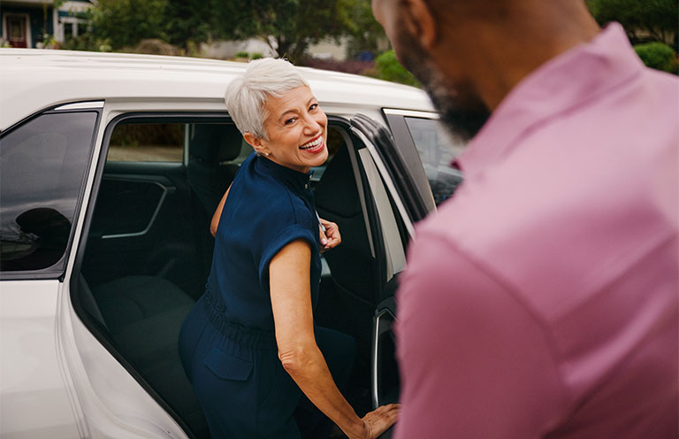 woman getting into back seat of car while she says bye to man standing outside of car