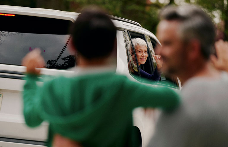 man and child waving bye to woman as she waves back from backseat of car