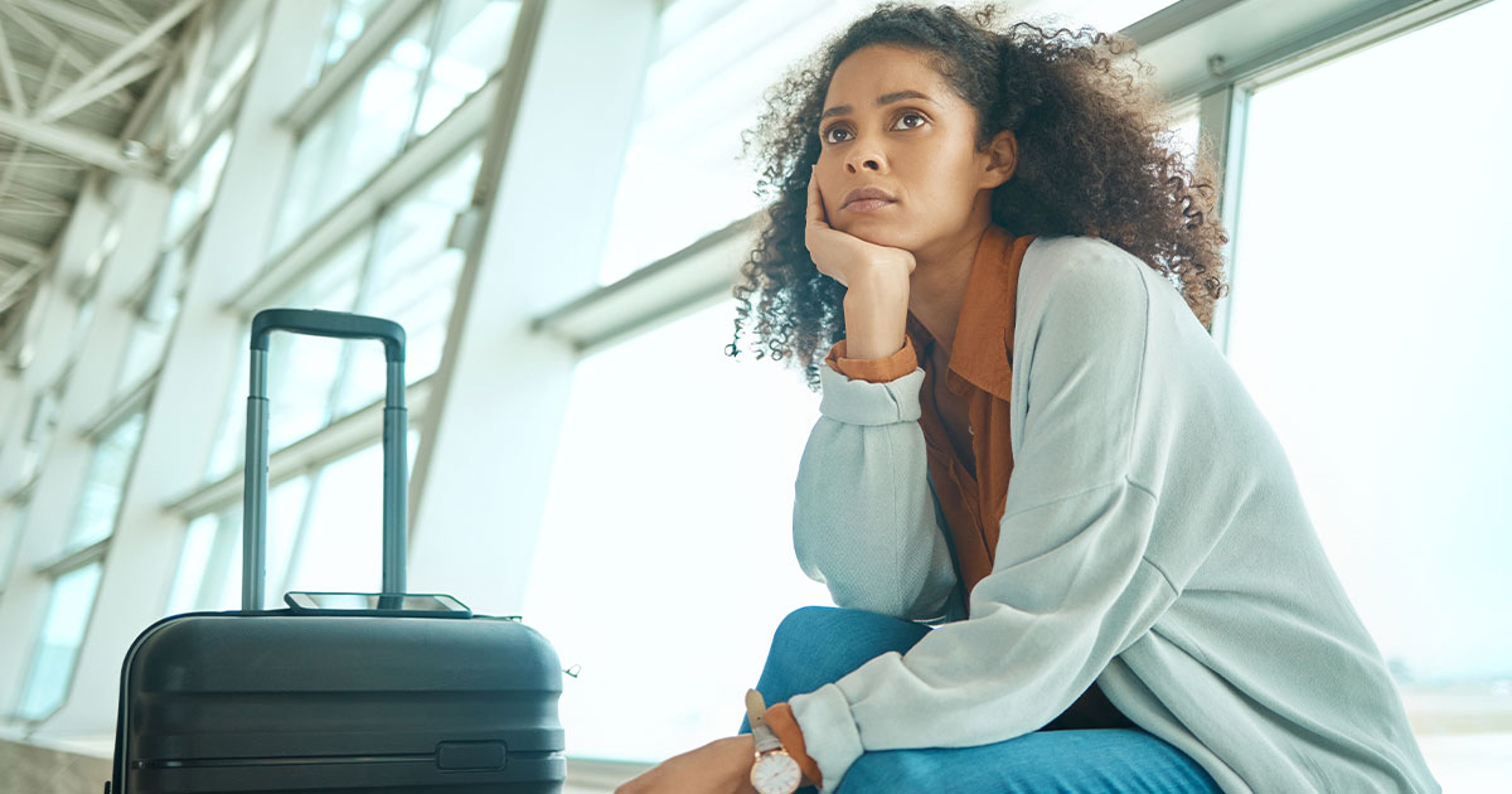 woman sitting with suitcase at airport, waiting for flight
