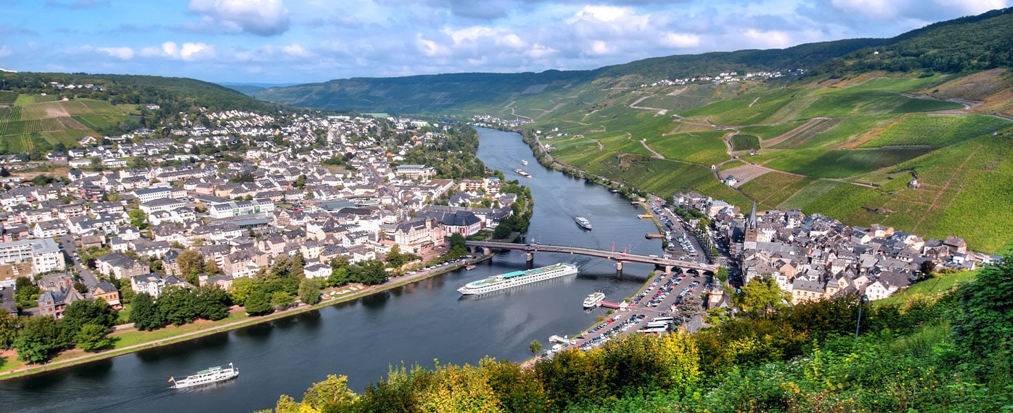A town surrounded by vineyards on the slopes of the river valley, tourist river boats can be seen traveling upriver