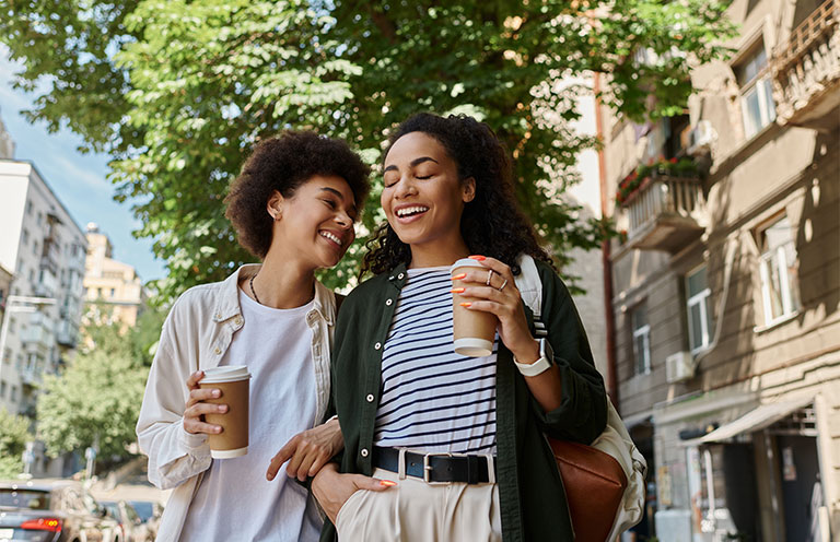 two women walking down the street with coffee cups