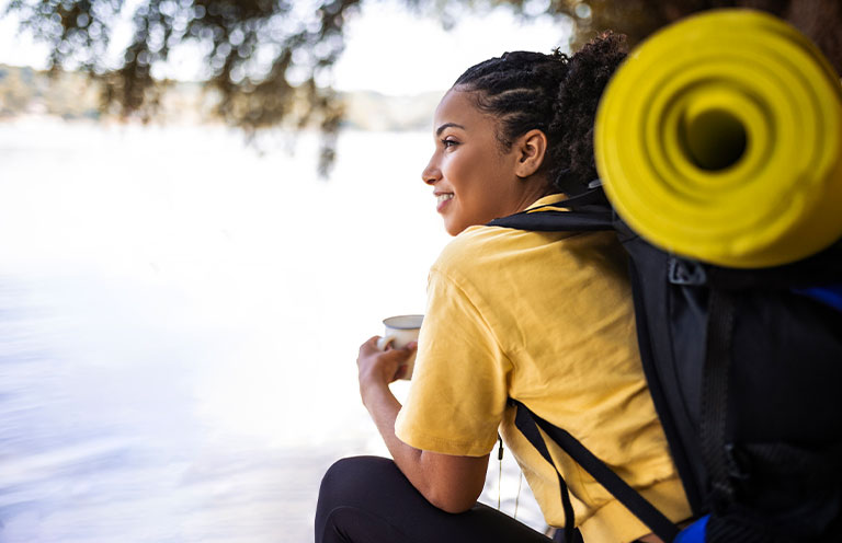 woman with camping gear holding mug by lake