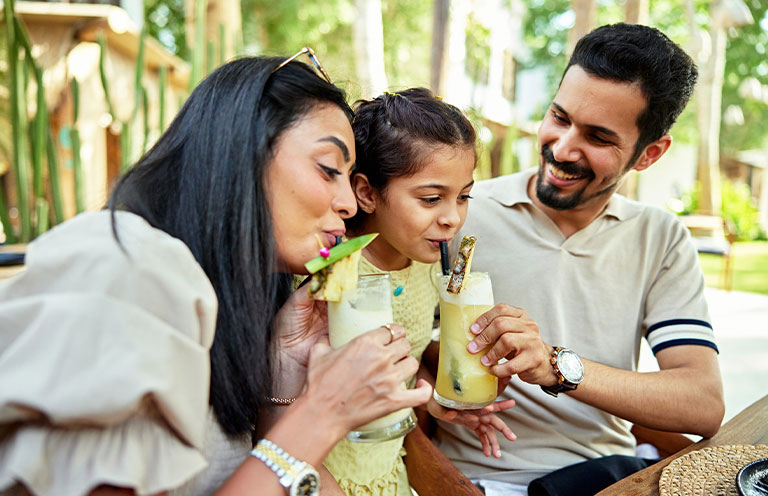 man and woman sharing pineapple smoothie with child