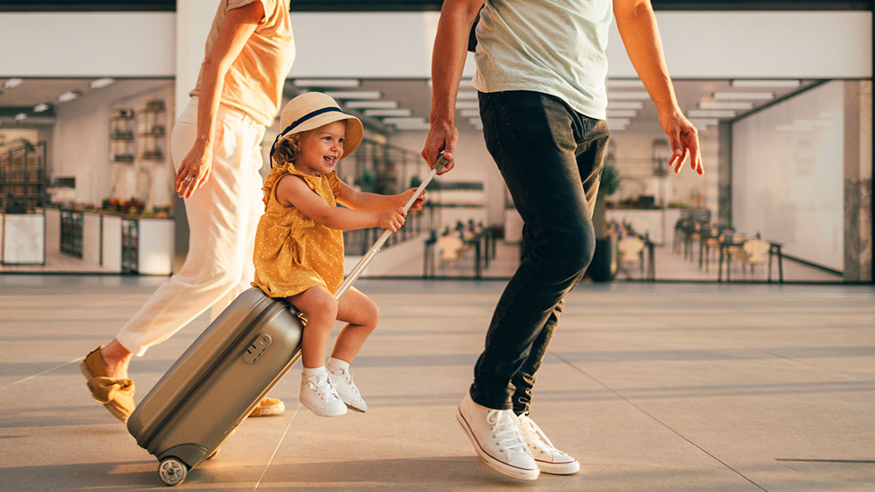 Husband and his wife walking with their little girl sitting on luggage at the airport