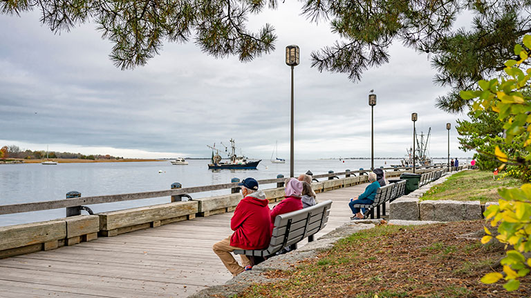 Elderly people breathe the fresh sea air while sitting on the wooden embankment of a small port town in New England on the Atlantic Ocean By vit