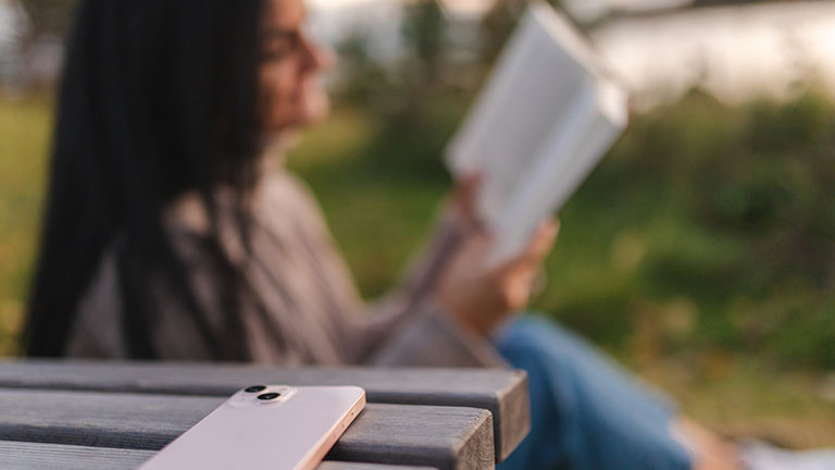Smart phone and a girl reading in the background; Credit: Luka Jankovic