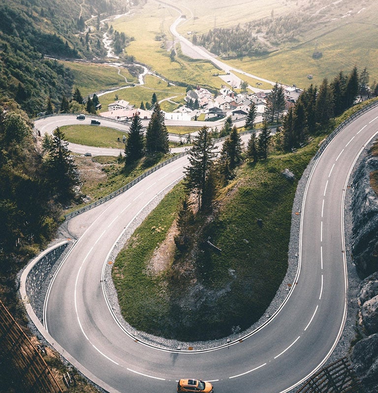 Cars make their way up the winding road of a steep mountain pass. A green valley can be seen beneath mist in the distance. Photo by Fabio Manuel Neto da luz from Burst
