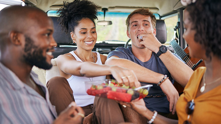 Diversity, fruit and friends on caravan road trip fruit while on holiday vacation eating watermelon, grapes and strawberry. Happy and hungry young men and women enjoying healthy fresh organic produce.  Credit: PeopleImages