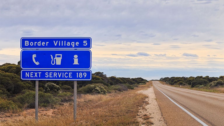 blue informational road sign in Western Australia about next service as well as perspective of Eyre Highway towards Border Village. Credit: zetter