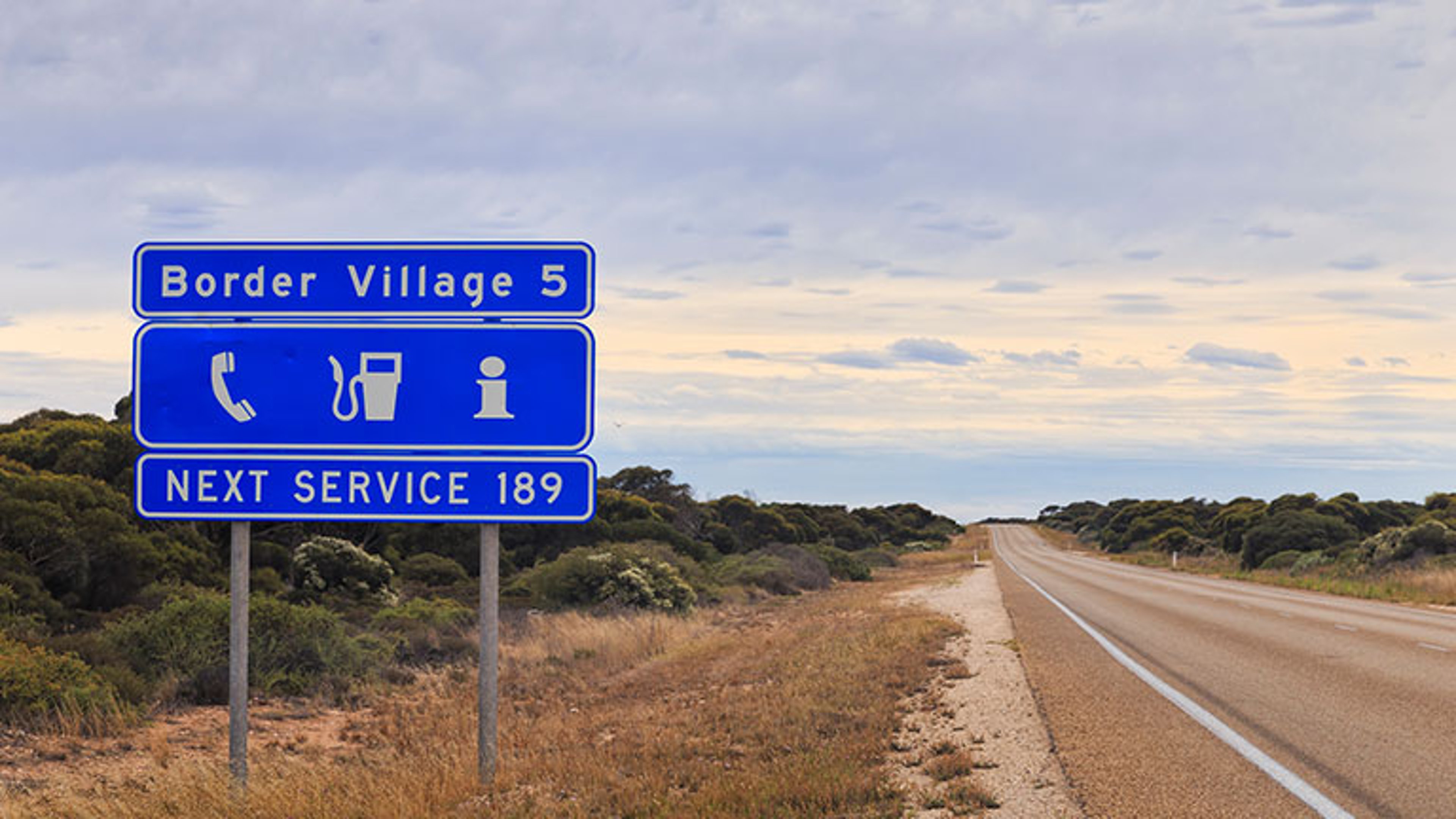 blue informational road sign in Western Australia about next service as well as perspective of Eyre Highway towards Border Village.  Credit: zetter