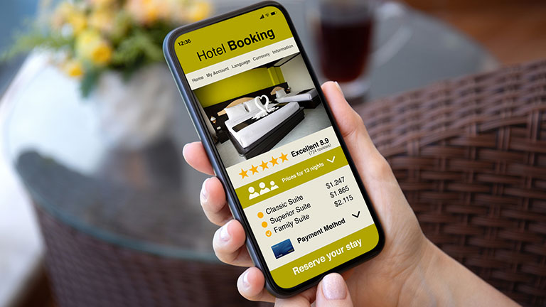 Man hand hold phone with hotel booking application background of table in café Credit:Prykhodov