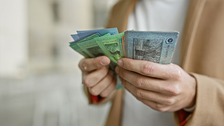 Young hispanic man counts malaysian ringgit on a busy city street, evoking themes of travel and finance.  by Krakenimages.com