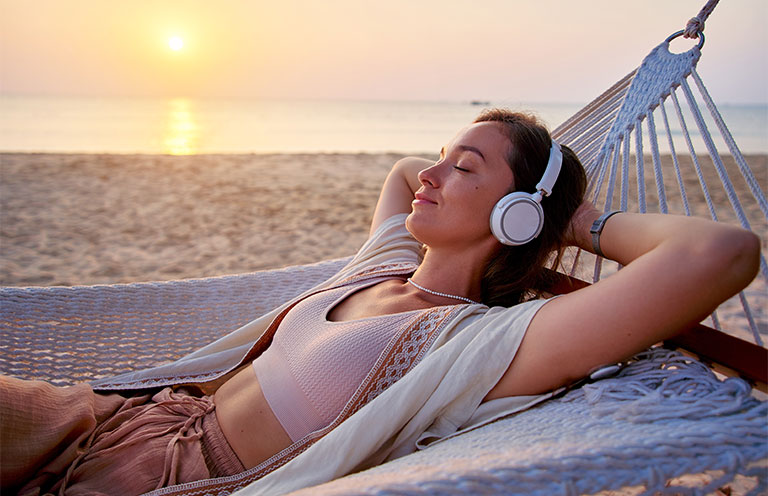 woman laying on hammock at beach wearing headphones