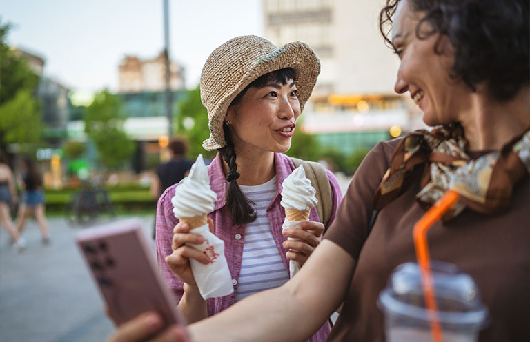 woman holding ice cream cones, other woman holding smoothie cup and taking selfie