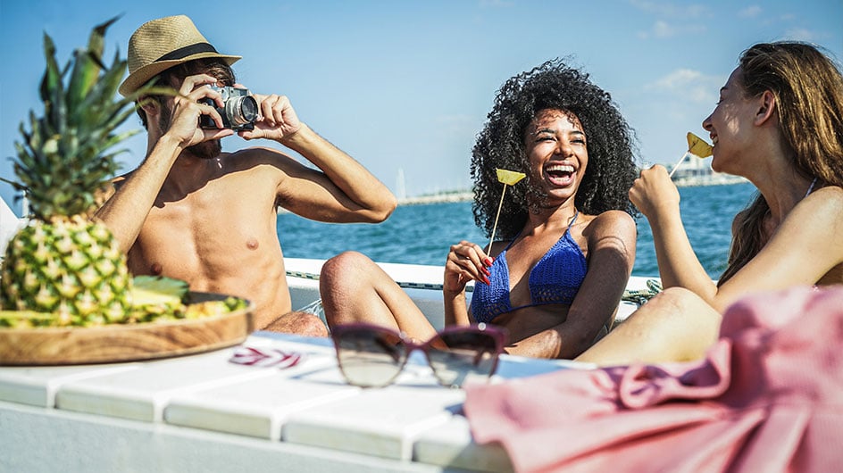 man takes picture of women eating fruit by water