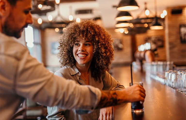 man placing drink in front of woman at the bar
